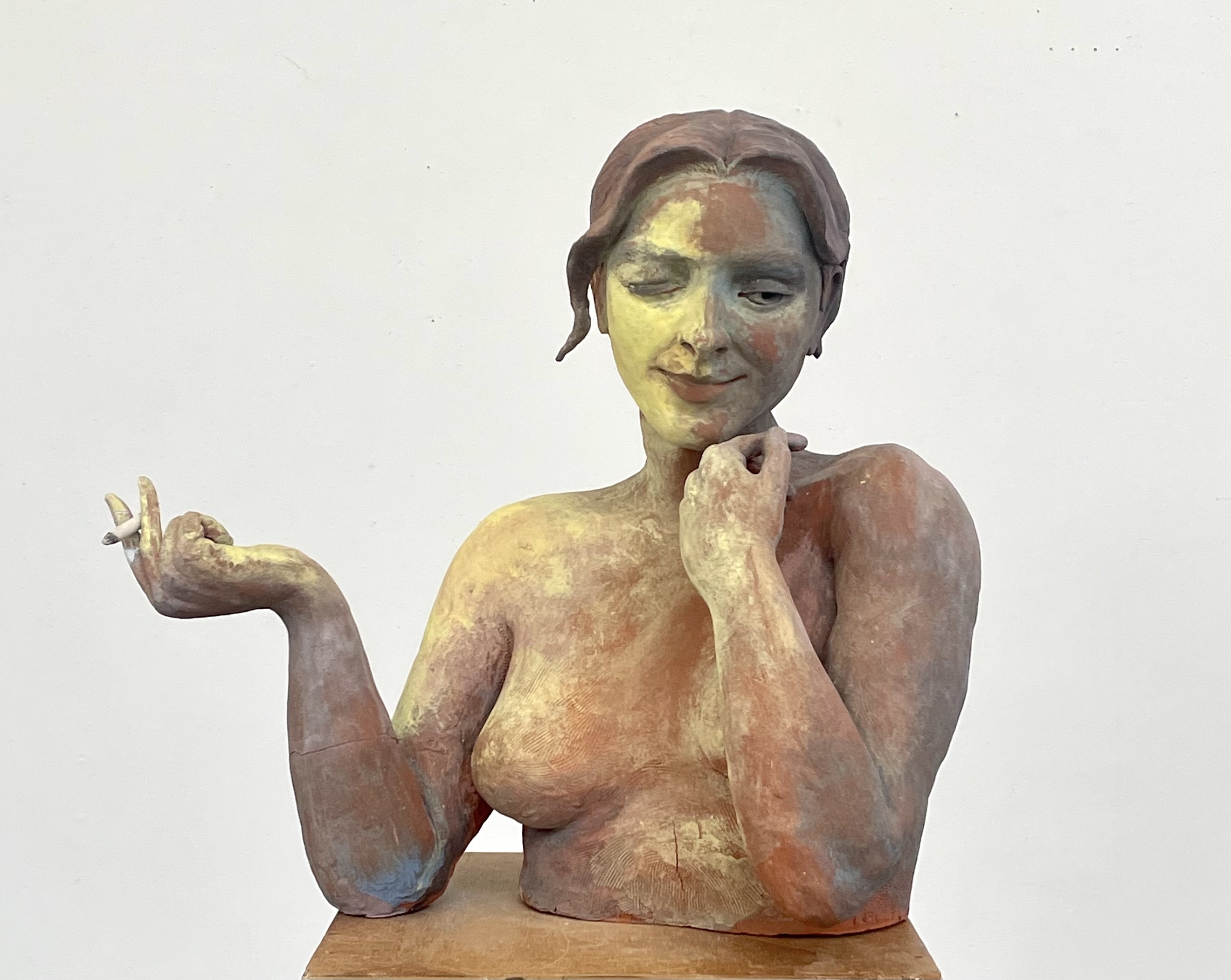 Painted ceramic self-portrait bust with one hand raised and the other resting under the chin